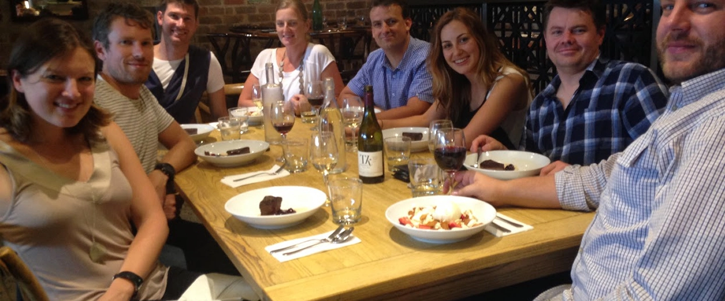 A diverse group of architects from Quattro Architecture gathered around a wooden dining table for a team dinner in a rustic restaurant setting.