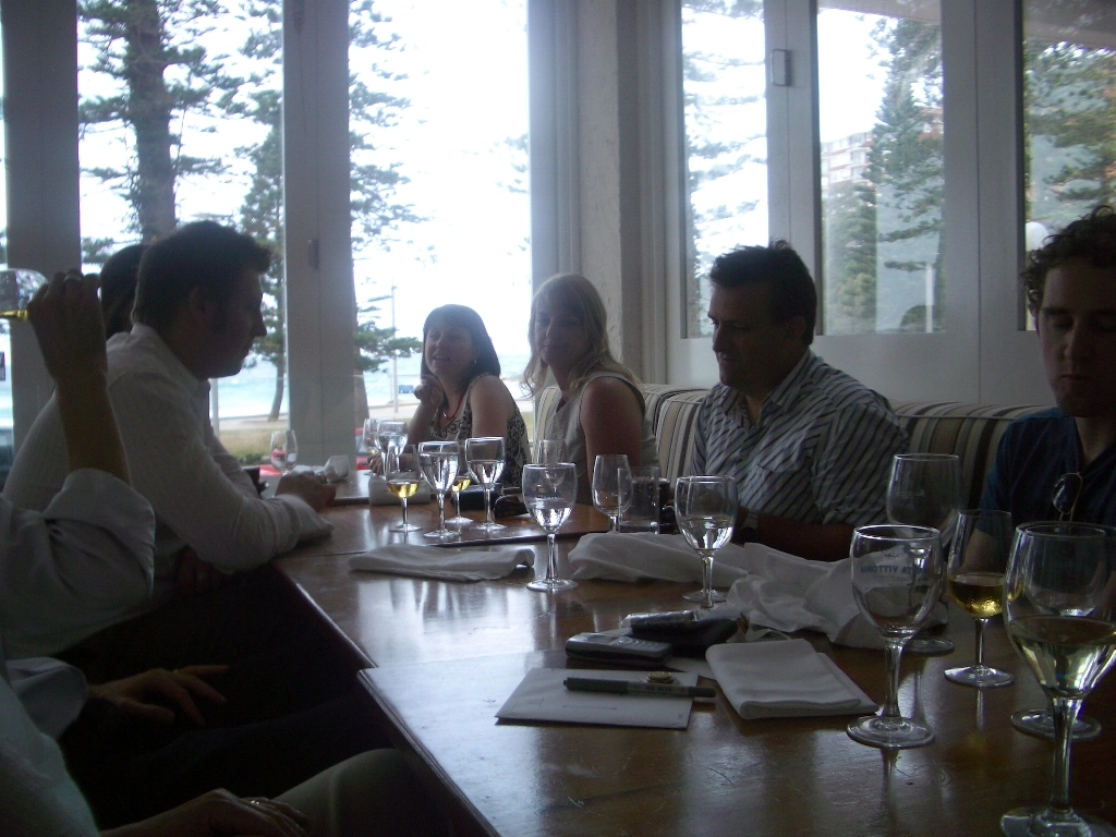 A group of colleagues from Quattro Architecture gathered around a wooden table for a professional lunch in a bright, sunlit dining space.