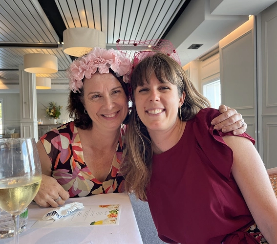Two women smiling at a Quattro Architecture team event, wearing festive headpieces in a modern interior with white paneled walls and pendant lights.