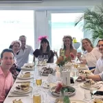 A group of colleagues from Quattro Architecture enjoying a celebratory lunch together in a bright, modern dining room with large windows.