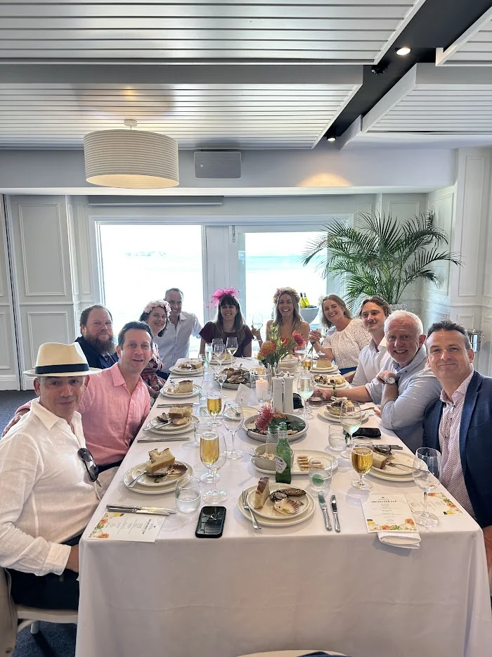 A group of colleagues from Quattro Architecture enjoying a celebratory lunch in a bright, modern dining room with large windows and coastal views.