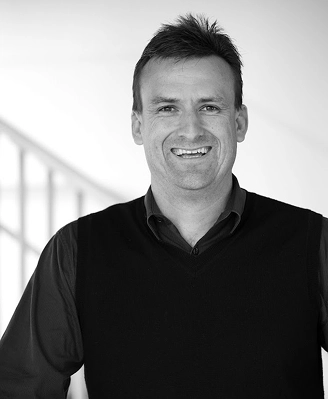 A black and white portrait of a smiling professional architect in a modern office, representing Quattro Architecture's design expertise since 2000.