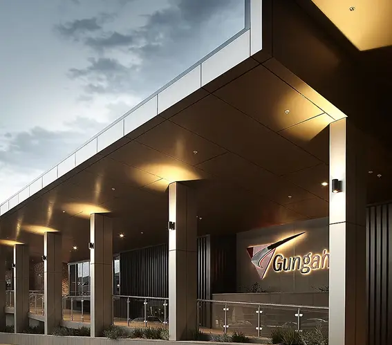 Modern commercial building entrance with sleek metal panels, warm recessed lighting, and a prominent illuminated sign under a wide canopy.